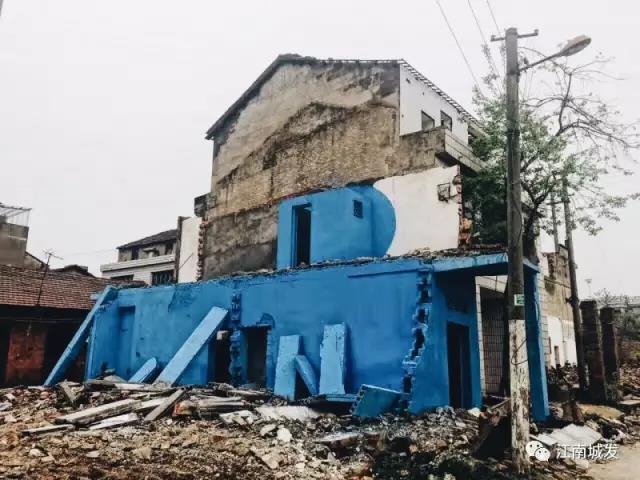 △ 這棟建筑是臨江最近的半拆遷建筑物的遺留，沅江和堤壩成為了展覽的天然背景。創(chuàng)作團(tuán)隊(duì)對(duì)這棟建筑進(jìn)行了半涂裝，將符號(hào)性的沅水曲線與拆遷進(jìn)行中的建筑立面進(jìn)行意義的疊造，它們共同觸發(fā)了場(chǎng)所空間多元語(yǔ)境的生成，把拆遷這種暫時(shí)破壞性、干擾性的介入行動(dòng)與沅水右岸發(fā)展的未來(lái)性、美好性緊密融合。